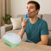 Man using an inhaler device with a green and white machine on a table in a living room setting.