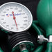 A close-up of a Dr. Odin manual blood pressure gauge with a green bulb, black rubber tubing, and a white dial face with black markings and a red needle.