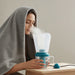 Woman using a humidifier with steam coming out, wrapped in a blanket.
