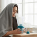 Person using a humidifier with a towel draped over their shoulders in a bright room.