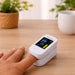 Finger pulse oximeter on a hand with a blurred background of a wooden table and plants.